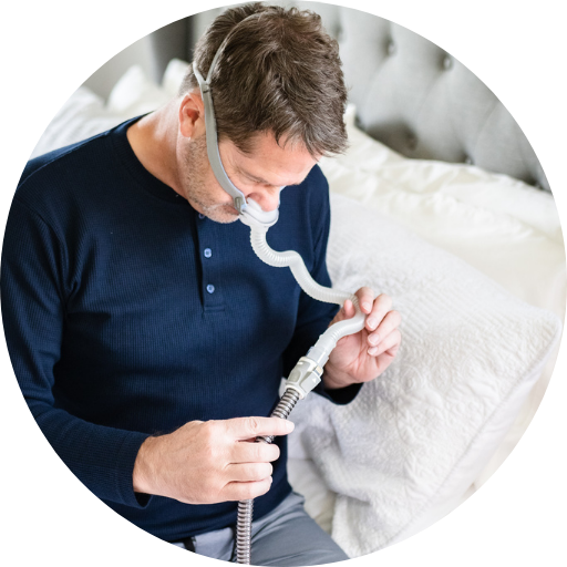 Man inspecting CPAP machine hose while wearing a nasal pillow CPAP mask