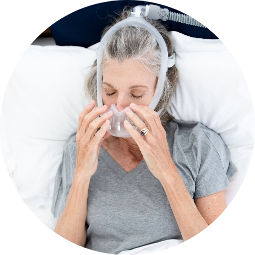 woman putting on a full face cpap mask while in bed