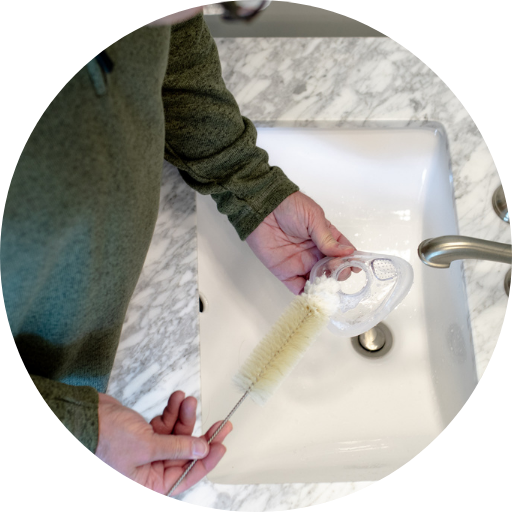man at a sink cleaning his full face cpap mask cushion using a cpap cleaning brush