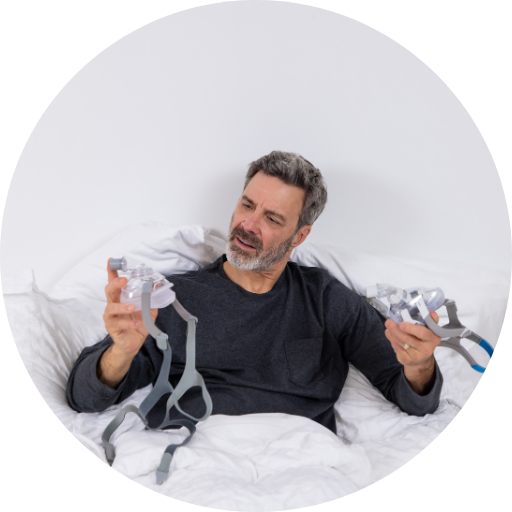 Man with a beard holding and inspecting two CPAP masks used for CPAP therapy to treat obstructive sleep apnea
