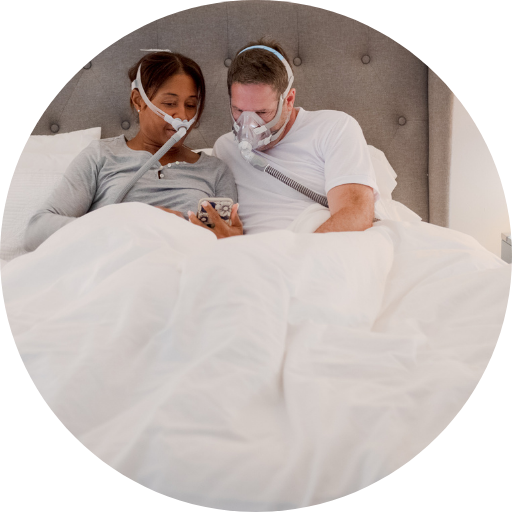 couple in bed wearing cpap masks on the phone