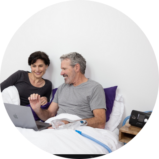 happy couple looking at the computer with a CPAP mask and a CPAP machine that is used for sleep apnea treatment
