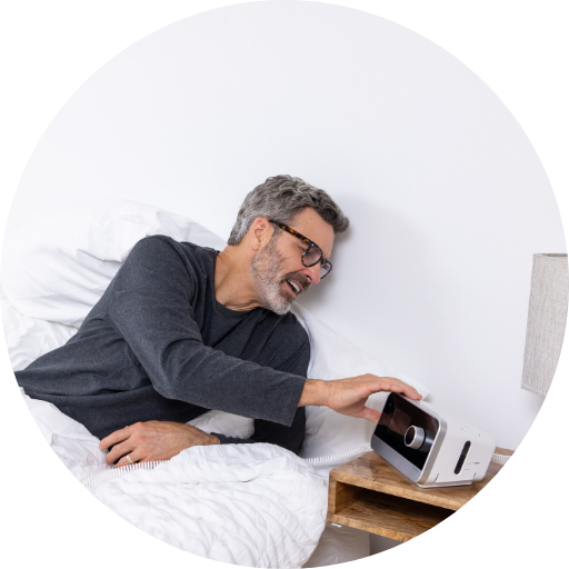 man laying in bed adjusting his CPAP machine settings