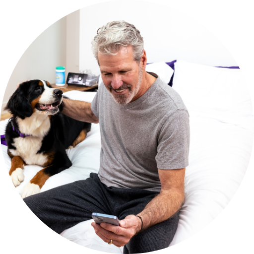 man on his phone and on the bed with a dog