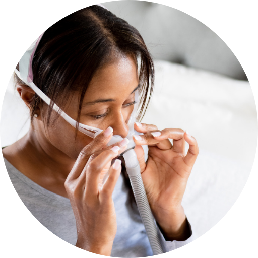 woman sitting on her bed putting on a nasal pillow cpap mask
