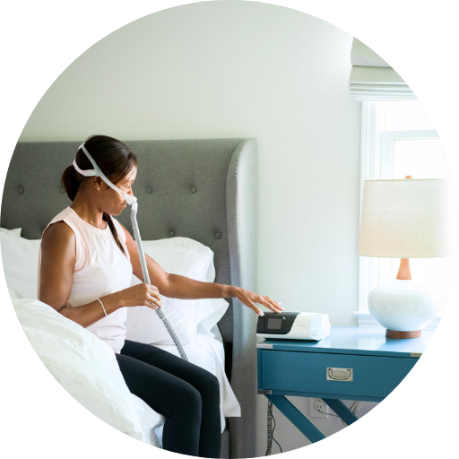 woman sitting on the bed wearing a CPAP mask adjusting the air pressure on a CPAP machine to treat sleep apnea